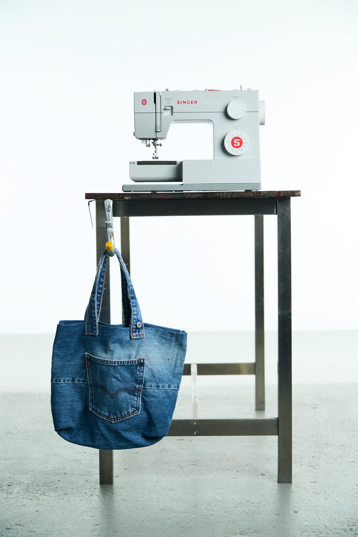 A finished denim tote hanging beside a sewing machine