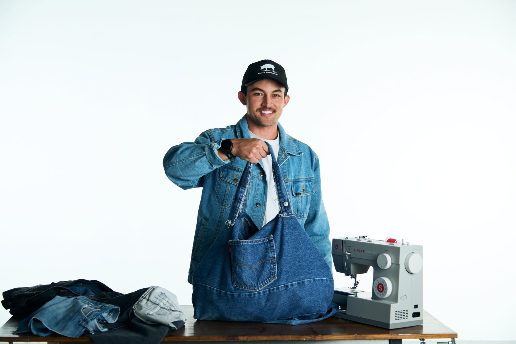 Maker holding a finished denim tote beside a sewing machine